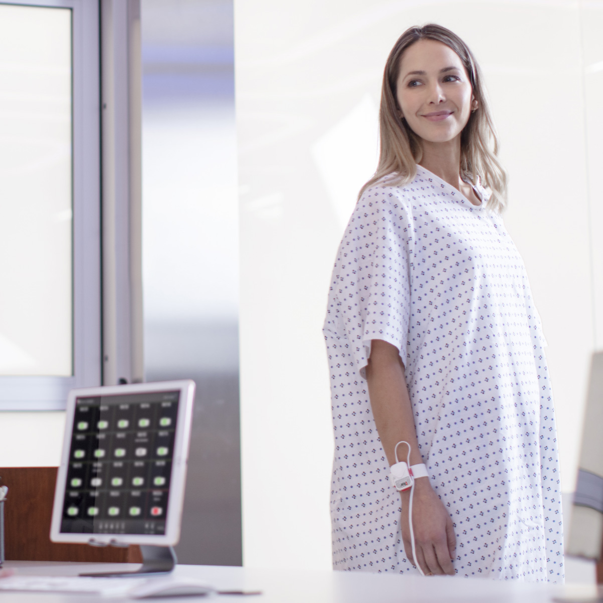 Patient standing in hospital near a central nursing station wearing a pulse oximetry sensor.